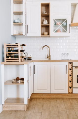 Modern kitchen design featuring white cabinets, wooden and stone countertops, a gold faucet, wine rack, open shelving, and a white subway tile backsplash.